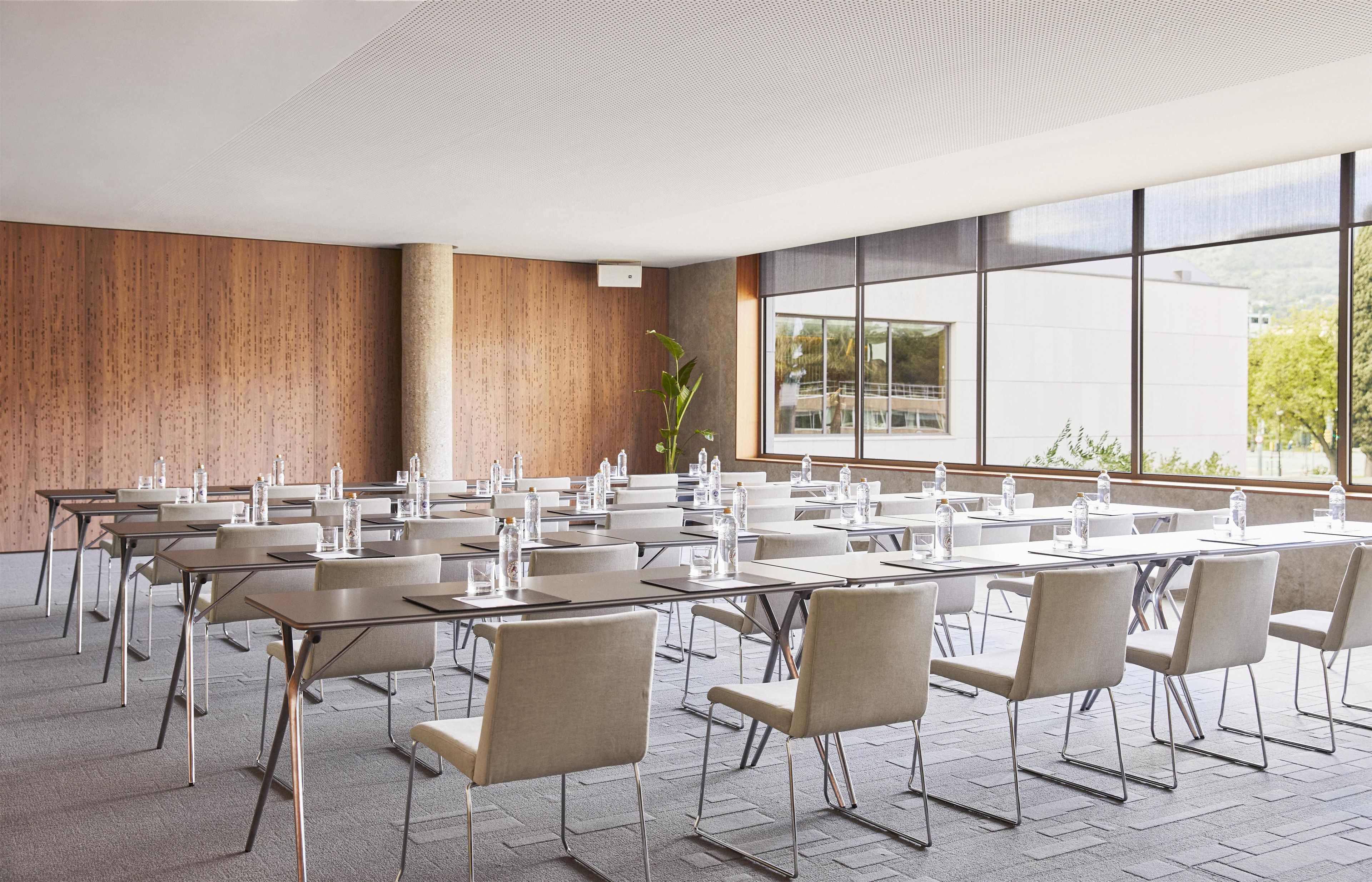 A conference room with multiple tables and chairs, large windows, and a wooden wall.