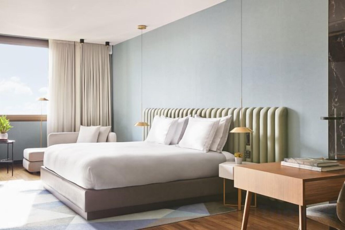 A modern bedroom with a large bed, bedside tables, a desk, and a window with curtains.