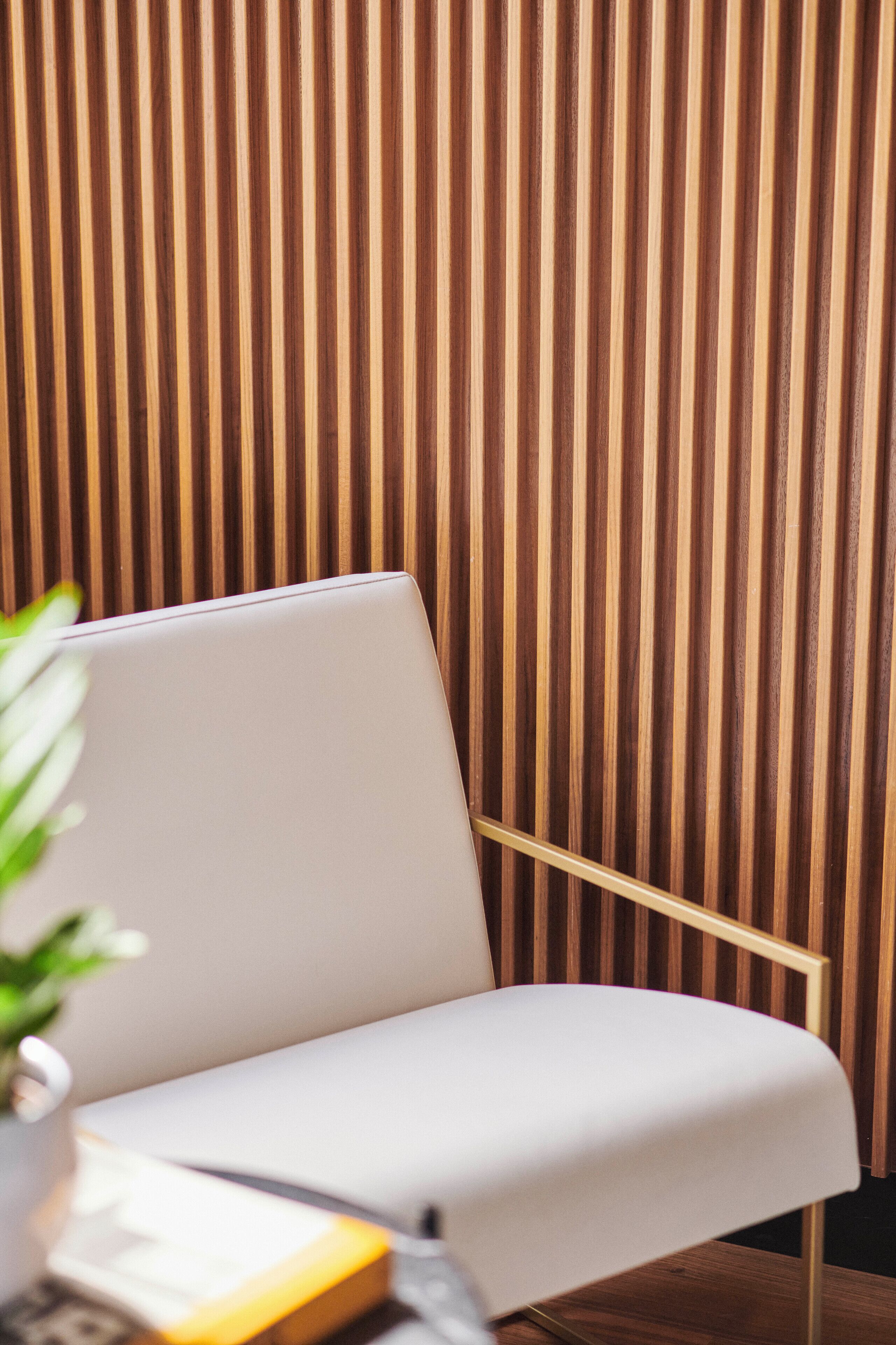 A modern room with a wooden slatted wall, a white chair, and a laptop on a wooden table.