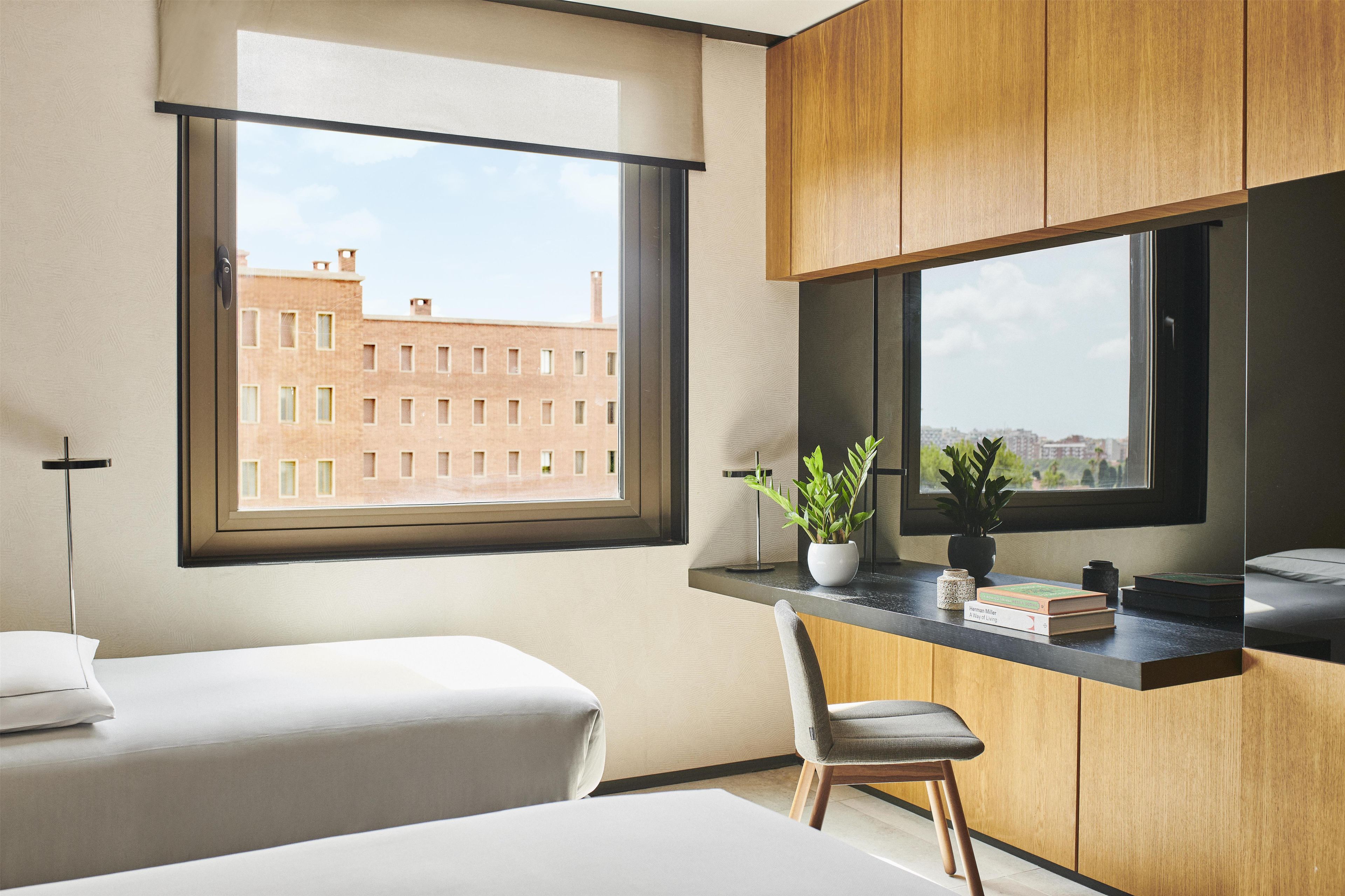 Una habitación de hotel moderna con un ventanal grande, un escritorio con silla y una cama.