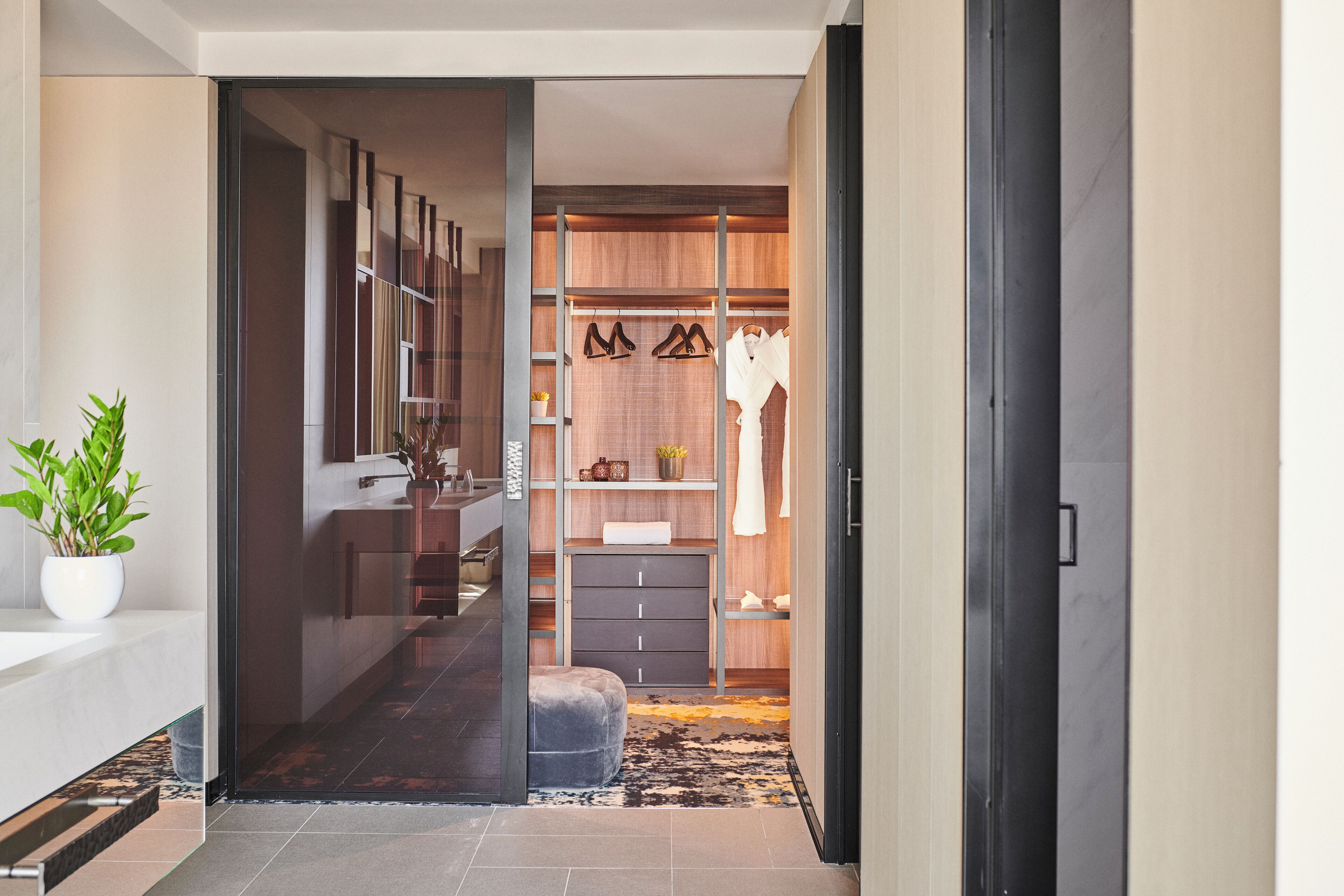 A modern hallway leading to a closet with a mirror, shelves, and a bench.