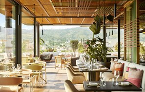 An outdoor dining area with tables and chairs, large windows, and a view of a mountainous landscape.