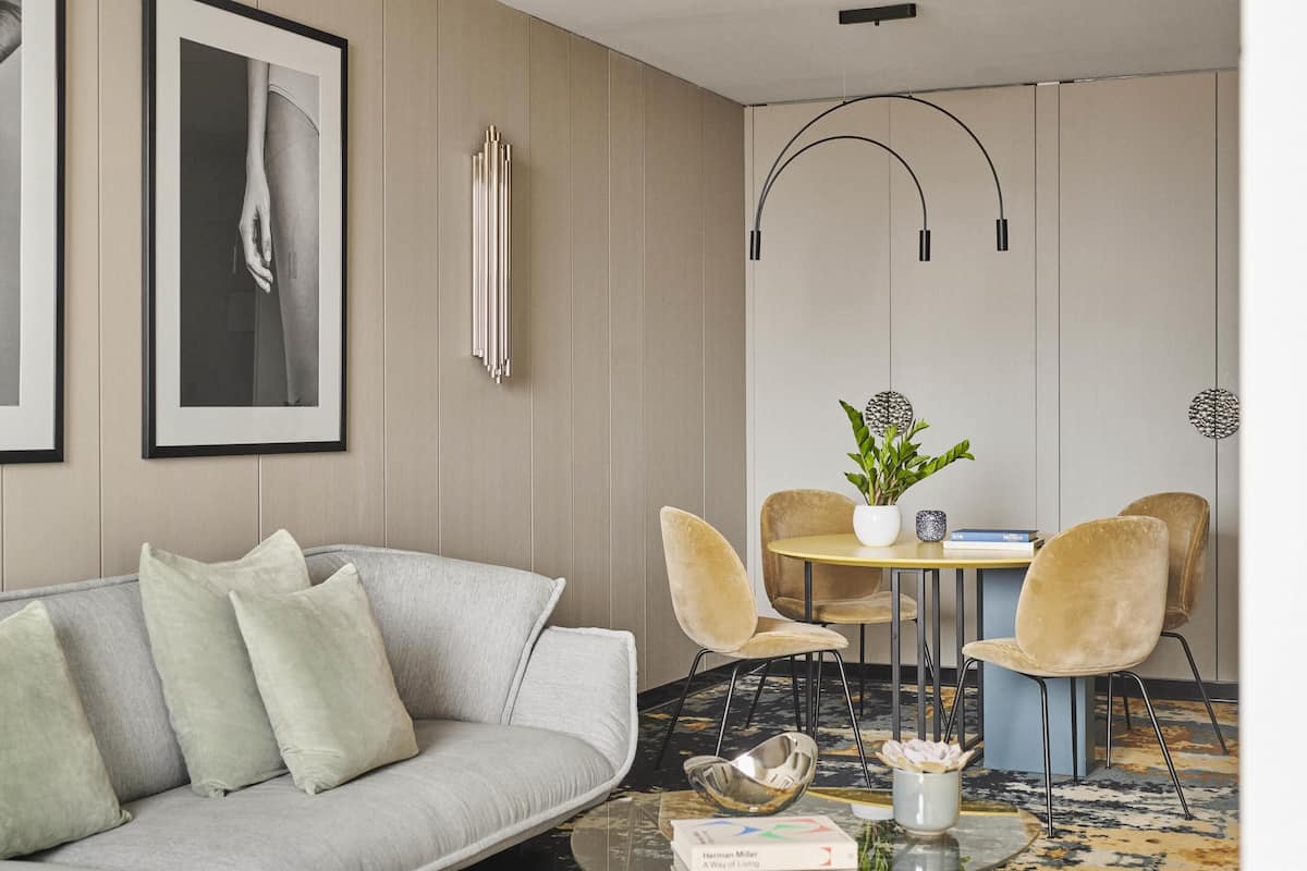 A modern living room with a grey sofa, a round table with chairs, and framed artwork on the wall.