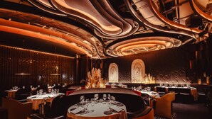 A modern restaurant with round tables, ambient lighting, and a decorative wall with a fire feature. - Grand Hyatt Barcelona (Barcelona)