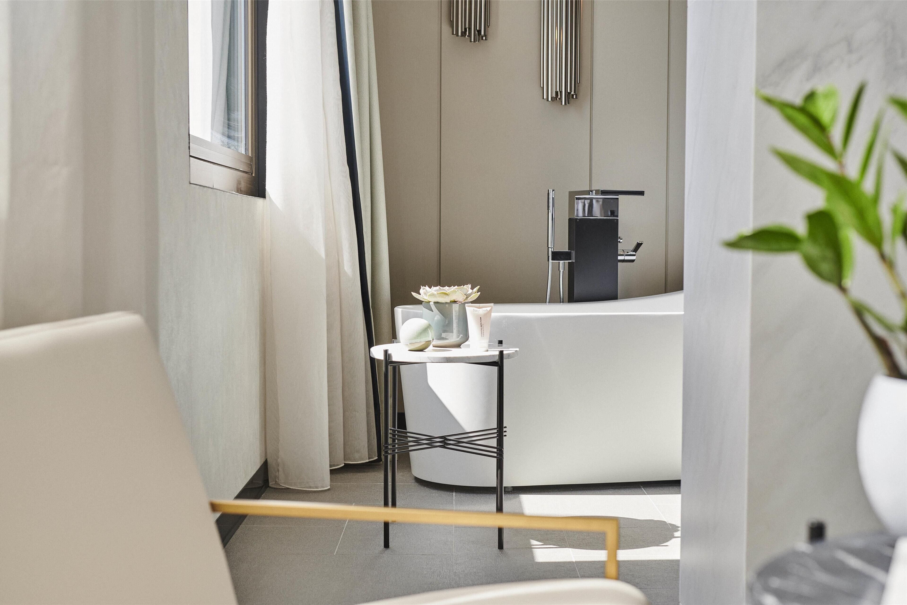 Une salle de bain moderne avec une baignoire, une petite table avec des articles de toilette et une plante.