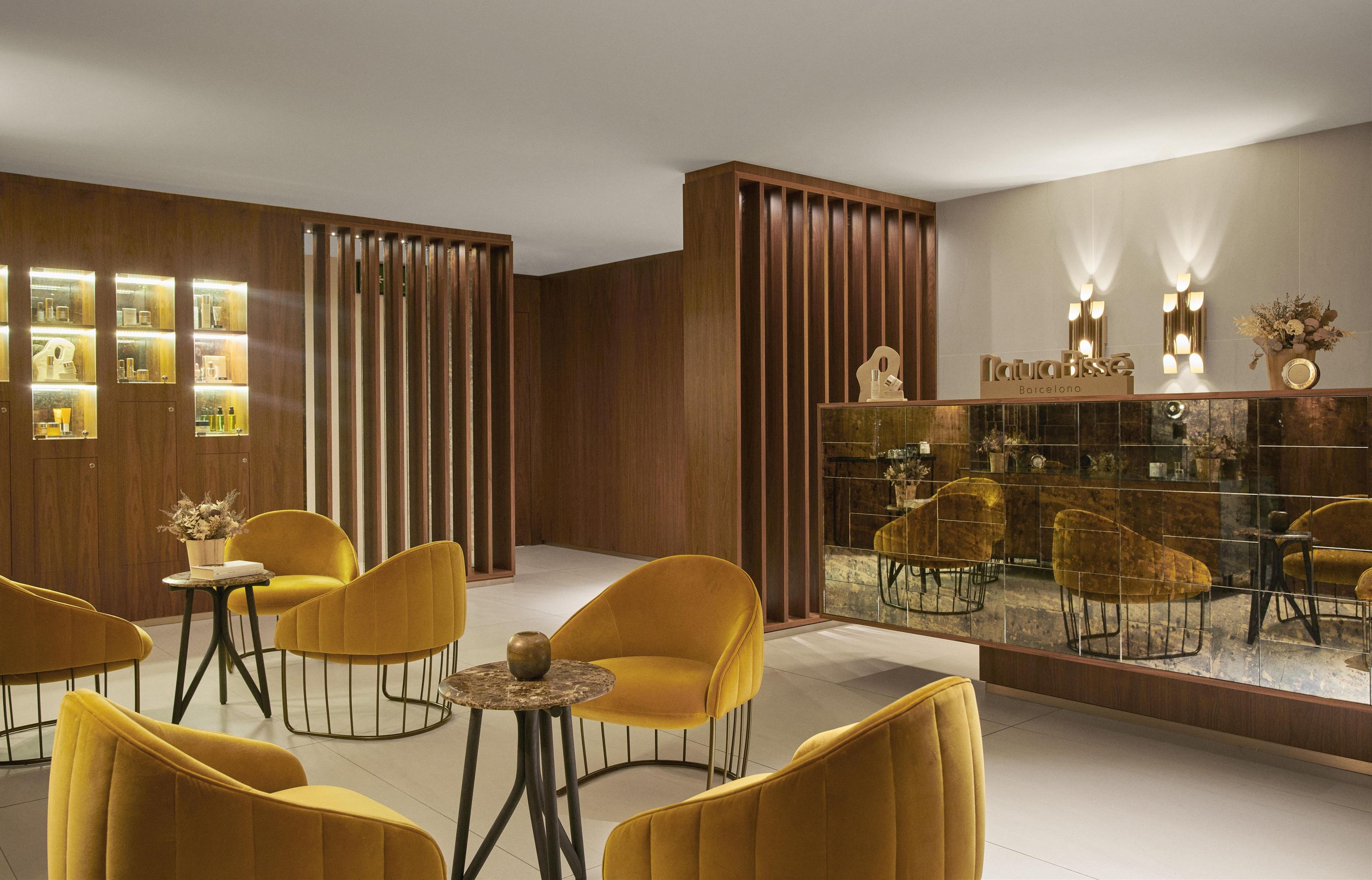 A modern interior with wooden paneling, yellow upholstered chairs, and a glass display case with a sign reading "Barcelona".