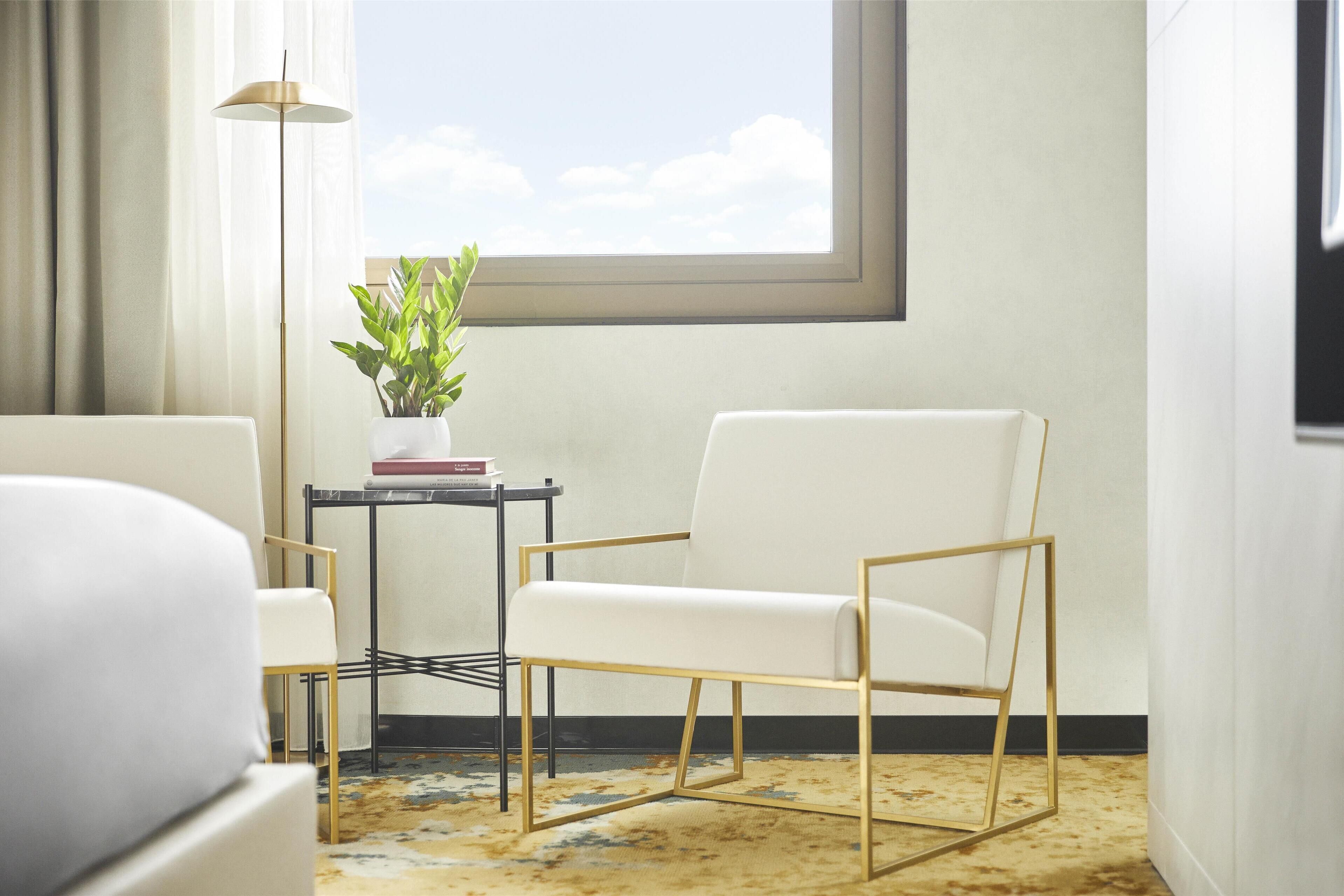 A modern room with a white armchair, a small table with a plant, and a floor lamp.