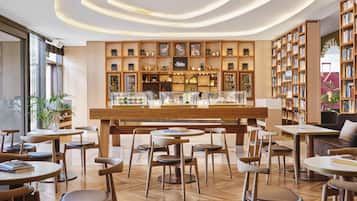 Un café moderno con mobiliario de madera, una barra central con vitrinas y estanterías llenas de libros.