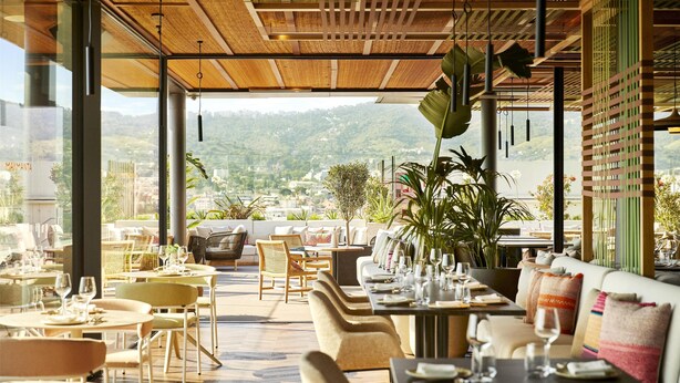 An outdoor dining area with tables and chairs, a large plant, and a view of a mountainous landscape. - Grand Hyatt Barcelona (Barcelona)