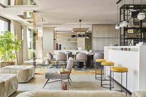 A modern living room with a dining area, featuring a sofa, chairs, a coffee table, and a bar area with stools.