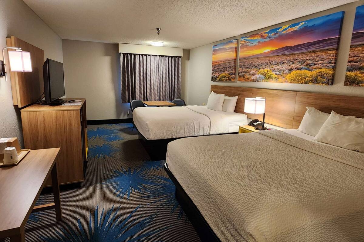 A hotel room with two beds, a desk, a television, and a painting of a sunset.