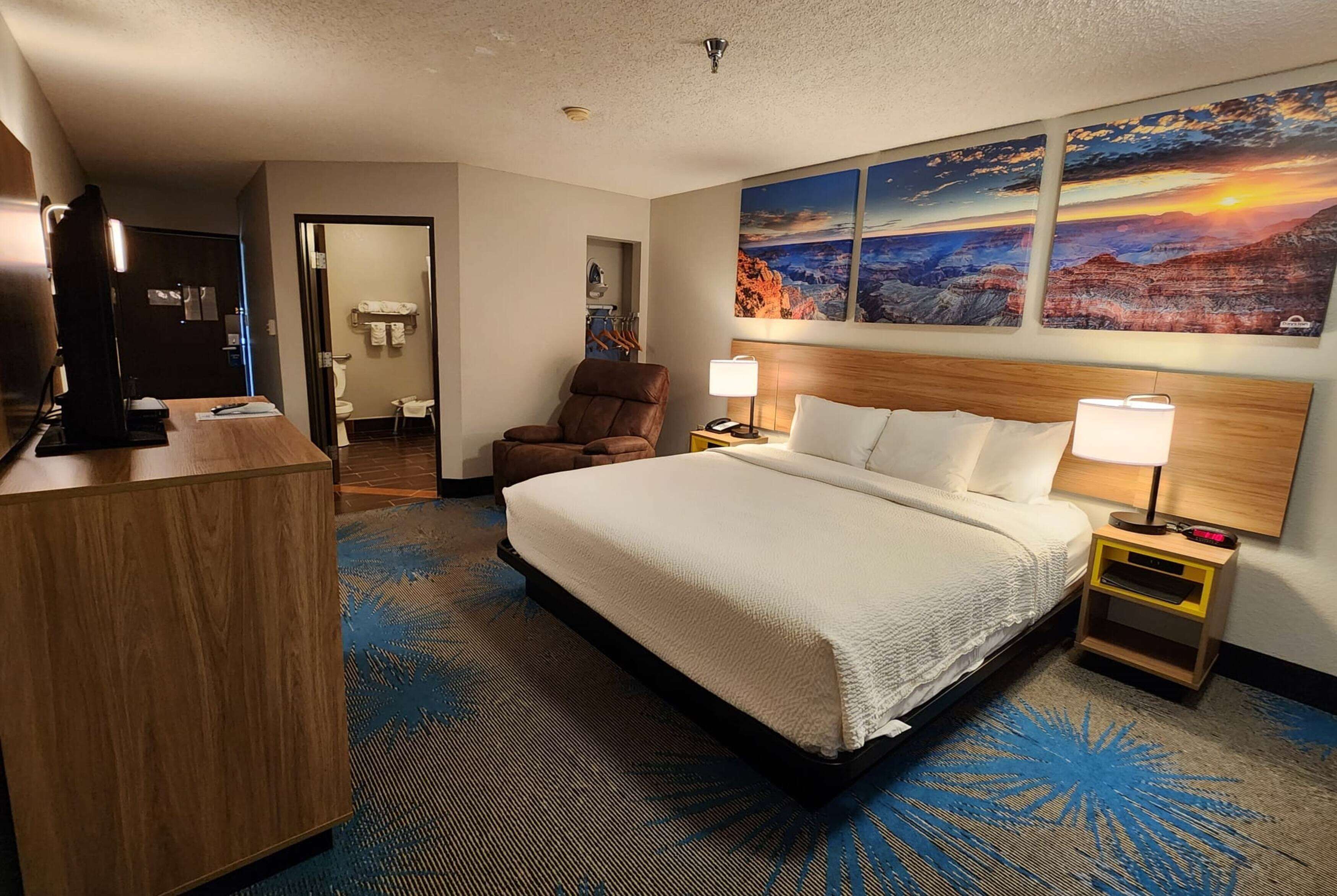 A hotel room with a large bed, a desk, a chair, and a painting of a mountain landscape.