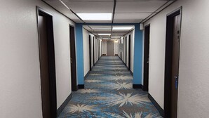 A hotel hallway with a patterned carpet, doors on both sides, and a ceiling with fluorescent lights.