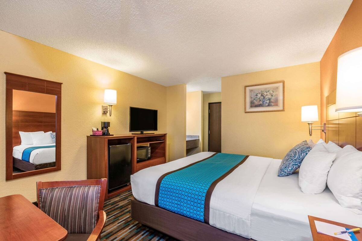A hotel room with a bed, a desk, a television, a microwave, and a door leading to another room.