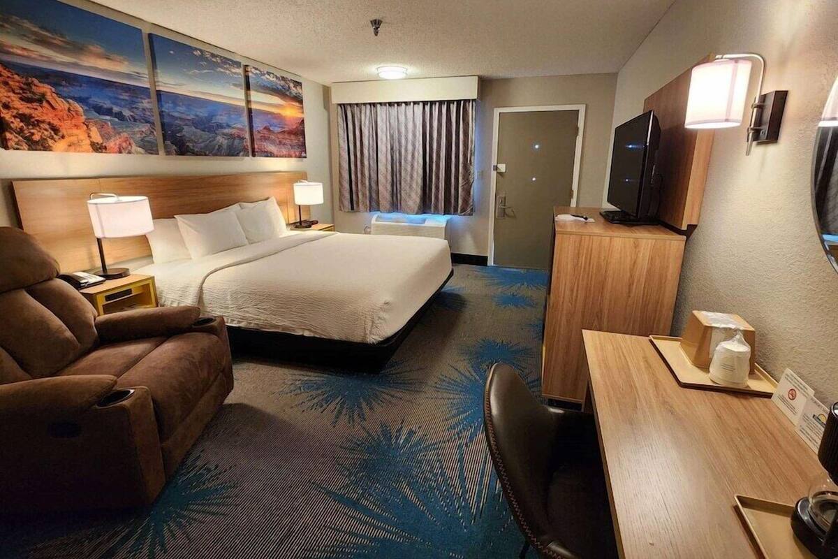 A hotel room with a bed, a desk, a chair, a TV, and a painting on the wall.