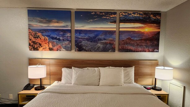 A hotel room with a large bed, two bedside tables with lamps, and three wall-mounted paintings of a canyon landscape.