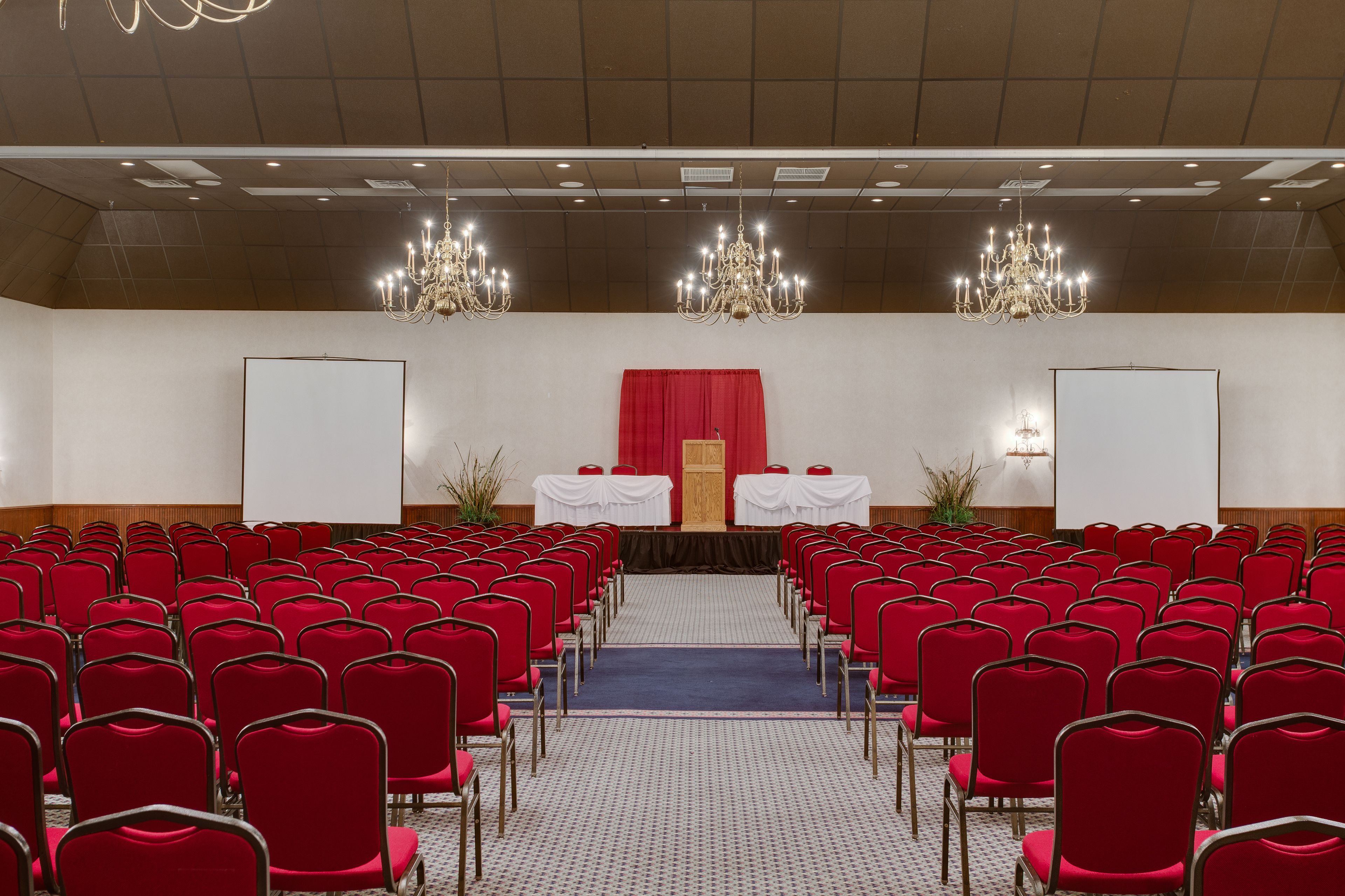 Ein Konferenzraum mit Reihen roter Stühle, einer Bühne mit rotem Vorhang und zwei Whiteboards.