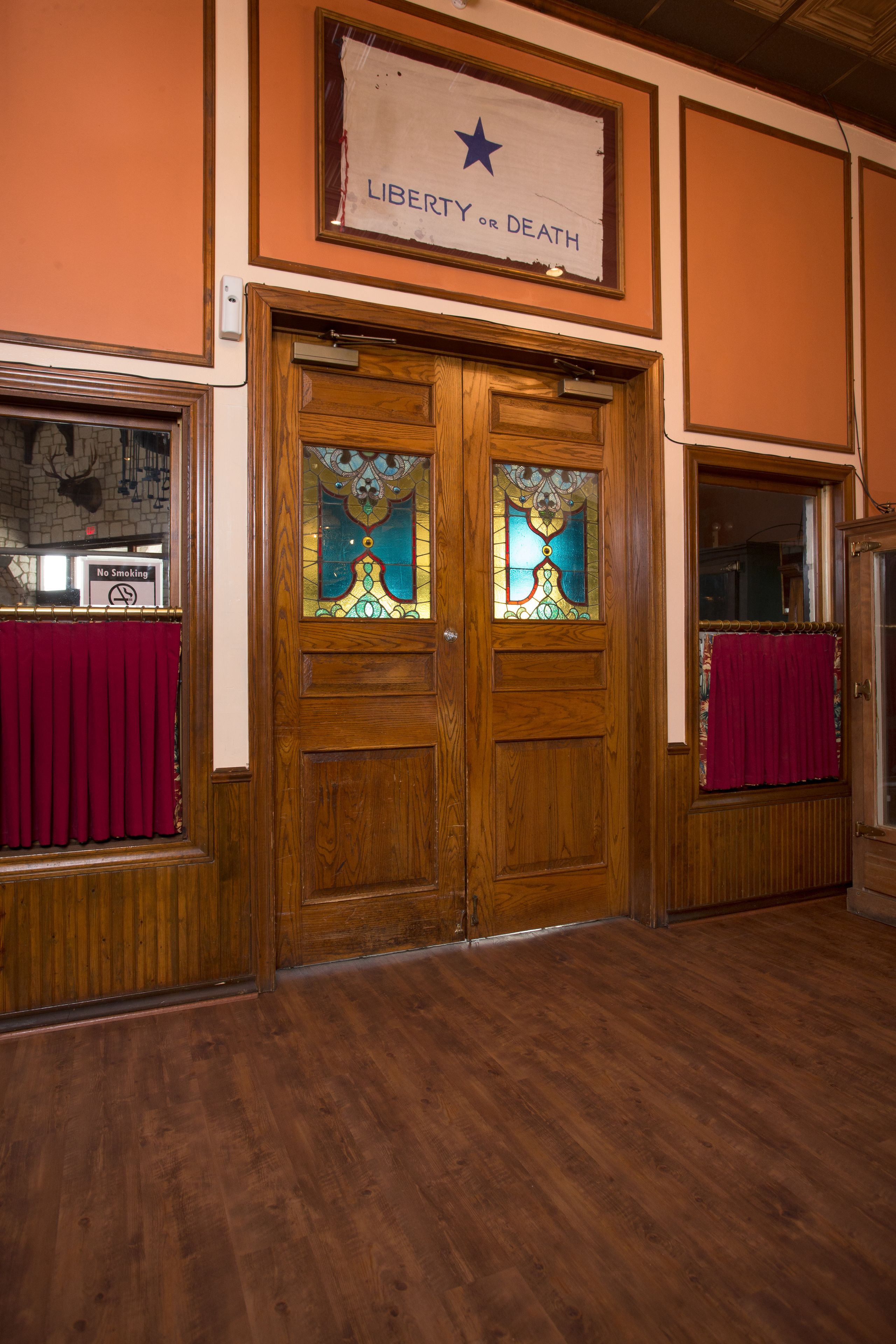 A wooden double door with stained glass windows and a sign above reading "Liberty or Death".