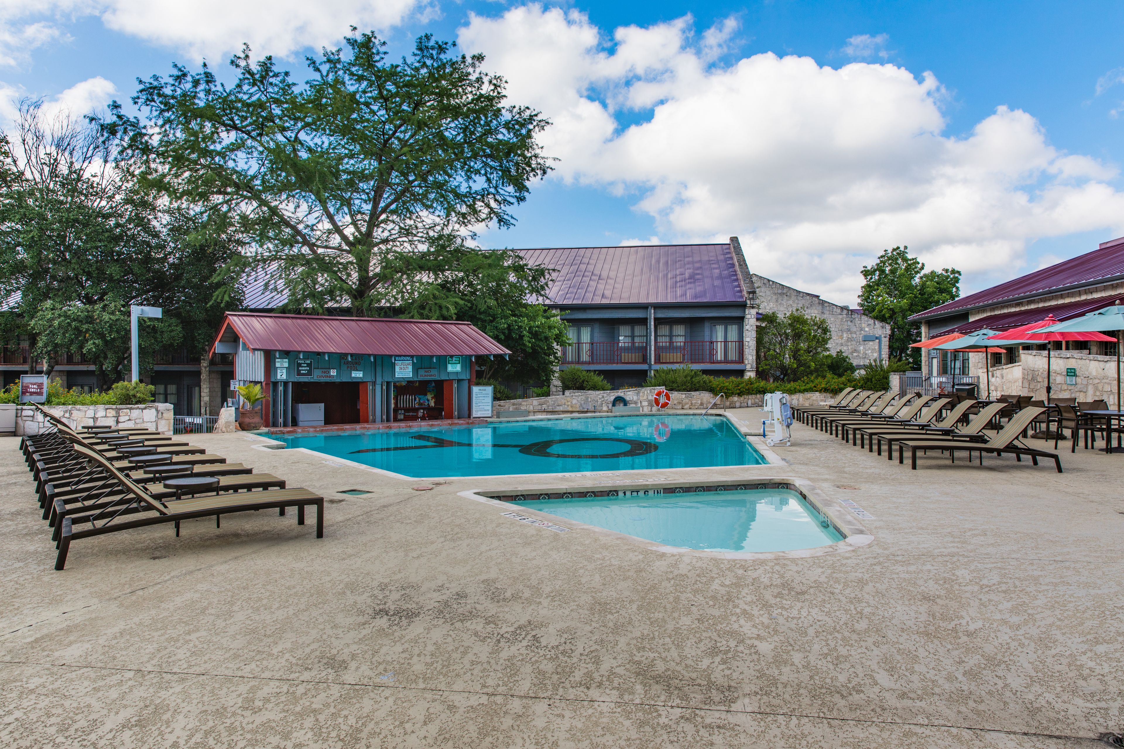 A swimming pool with lounge chairs, a lifeguard stand, and a building with a red roof.