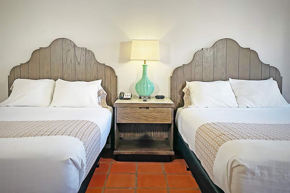 A hotel room with two beds, a nightstand with a lamp, and a phone.
