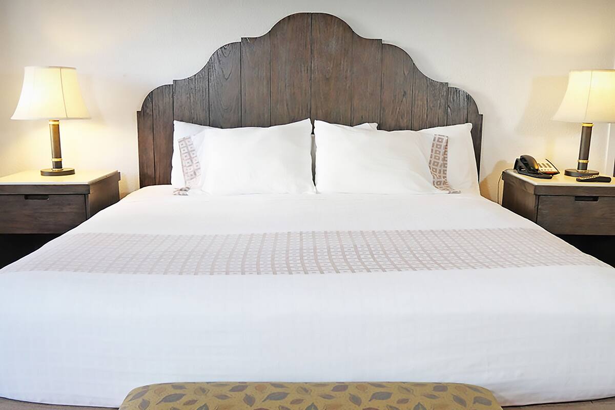 A large bed with a wooden headboard, two bedside tables with lamps, and a patterned ottoman.