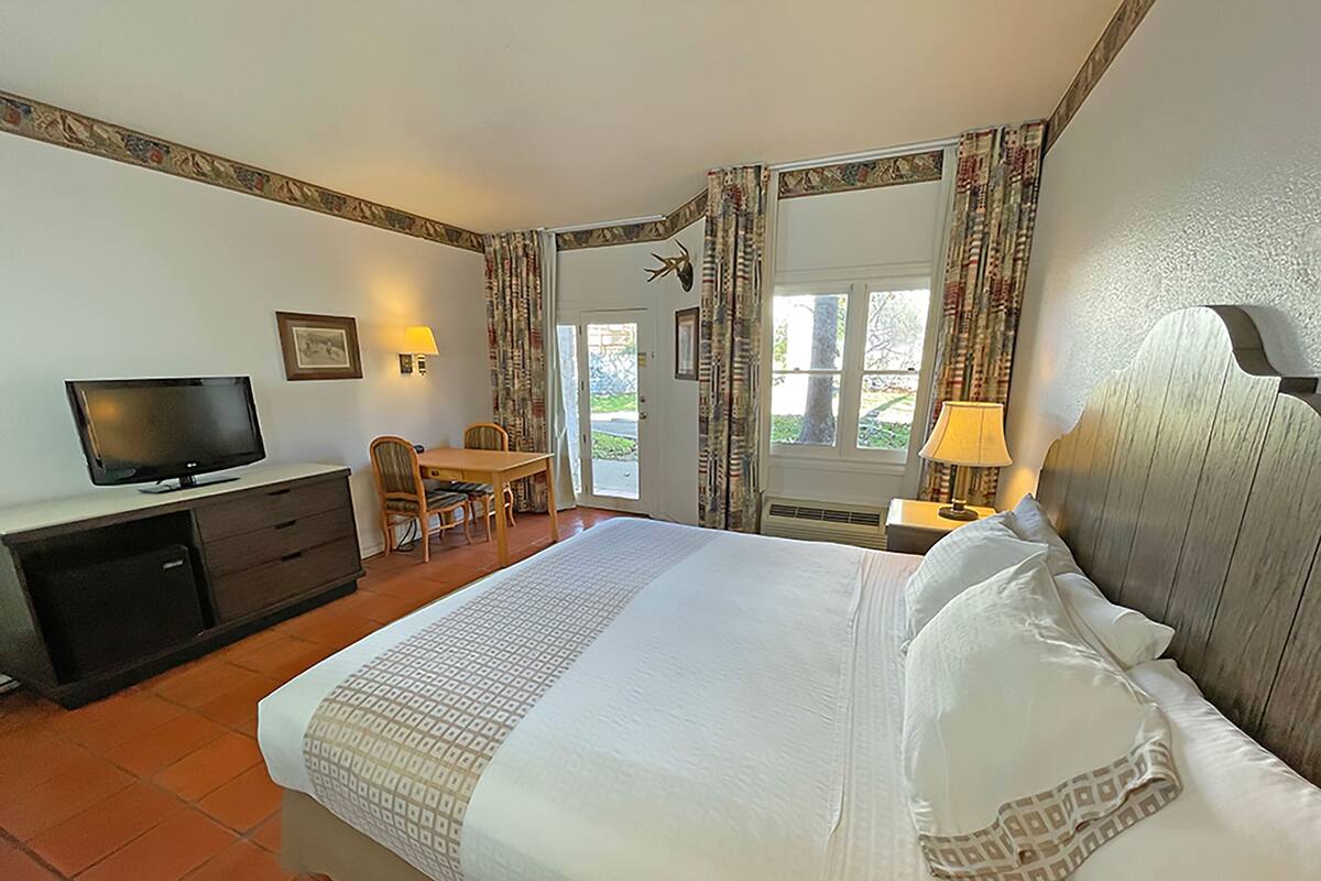 A hotel room with a bed, a desk, a television, and a window with curtains.