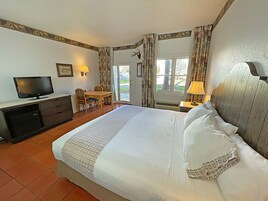 A hotel room with a bed, a desk, a television, and a window with curtains.