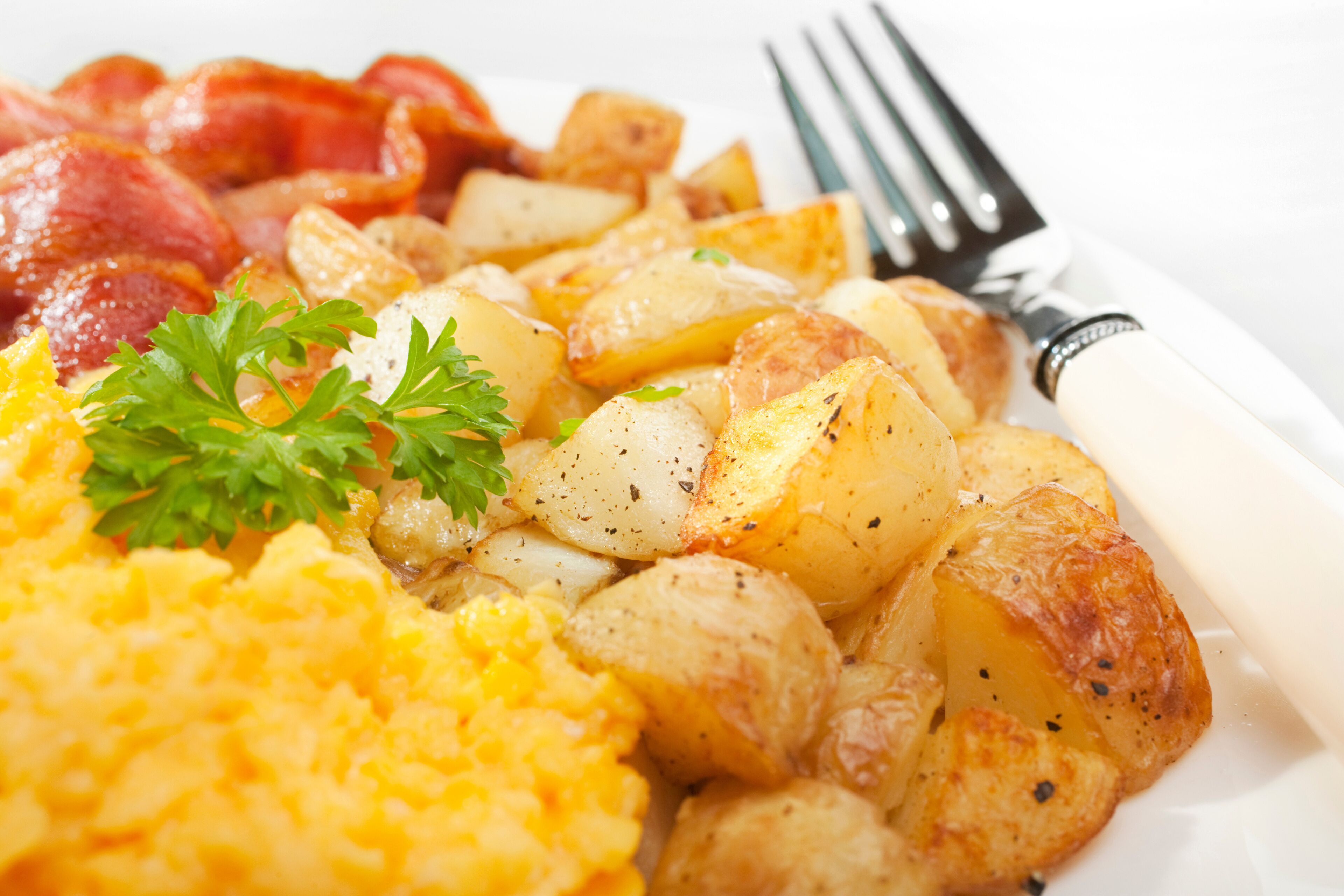 A plate of scrambled eggs, roasted potatoes, and bacon.