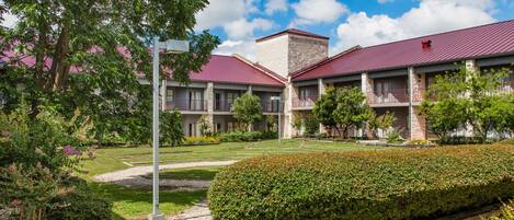 A hotel with a red roof, multiple balconies, and a well-maintained garden with hedges and trees.