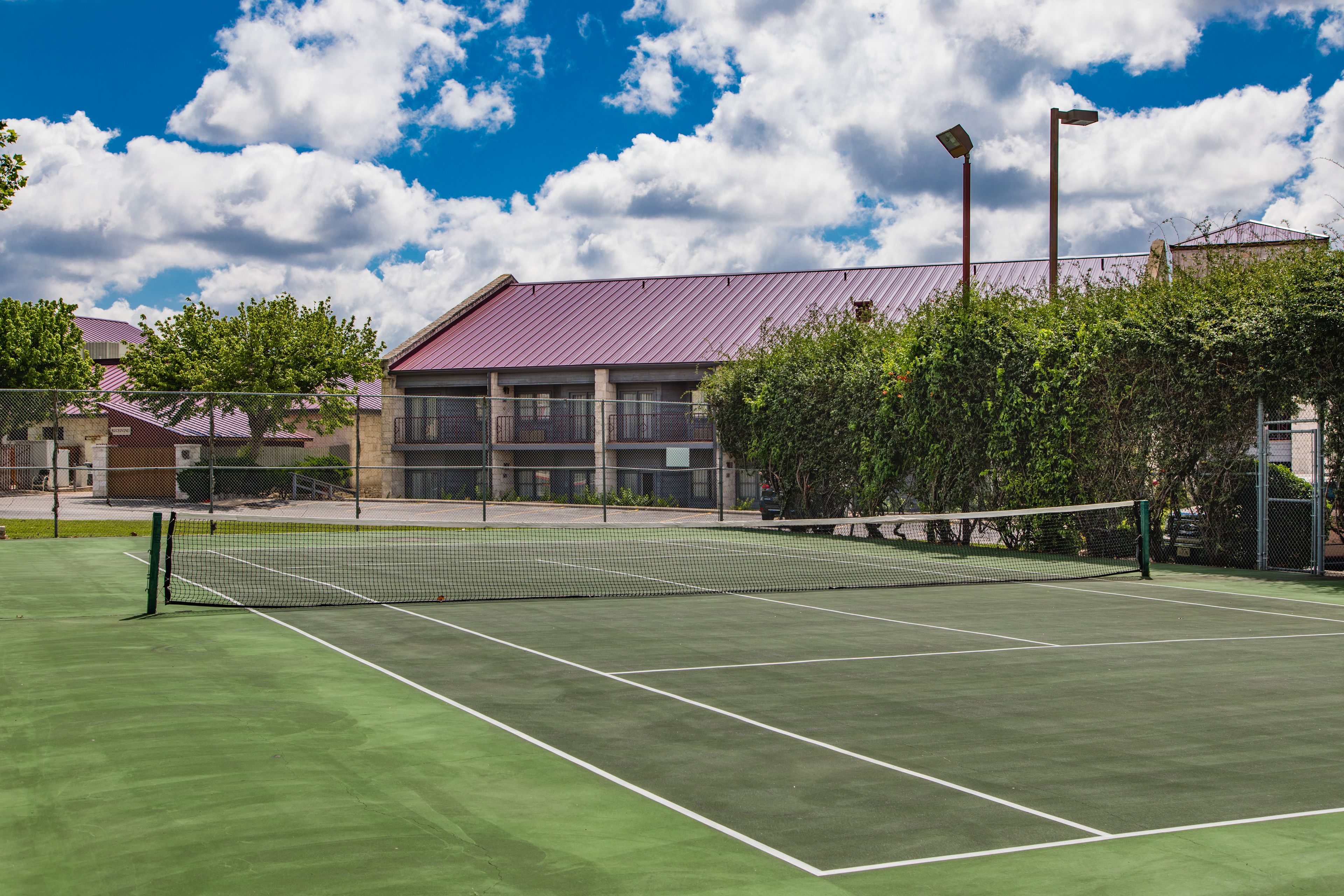 A tennis court with a net, surrounded by trees and buildings.