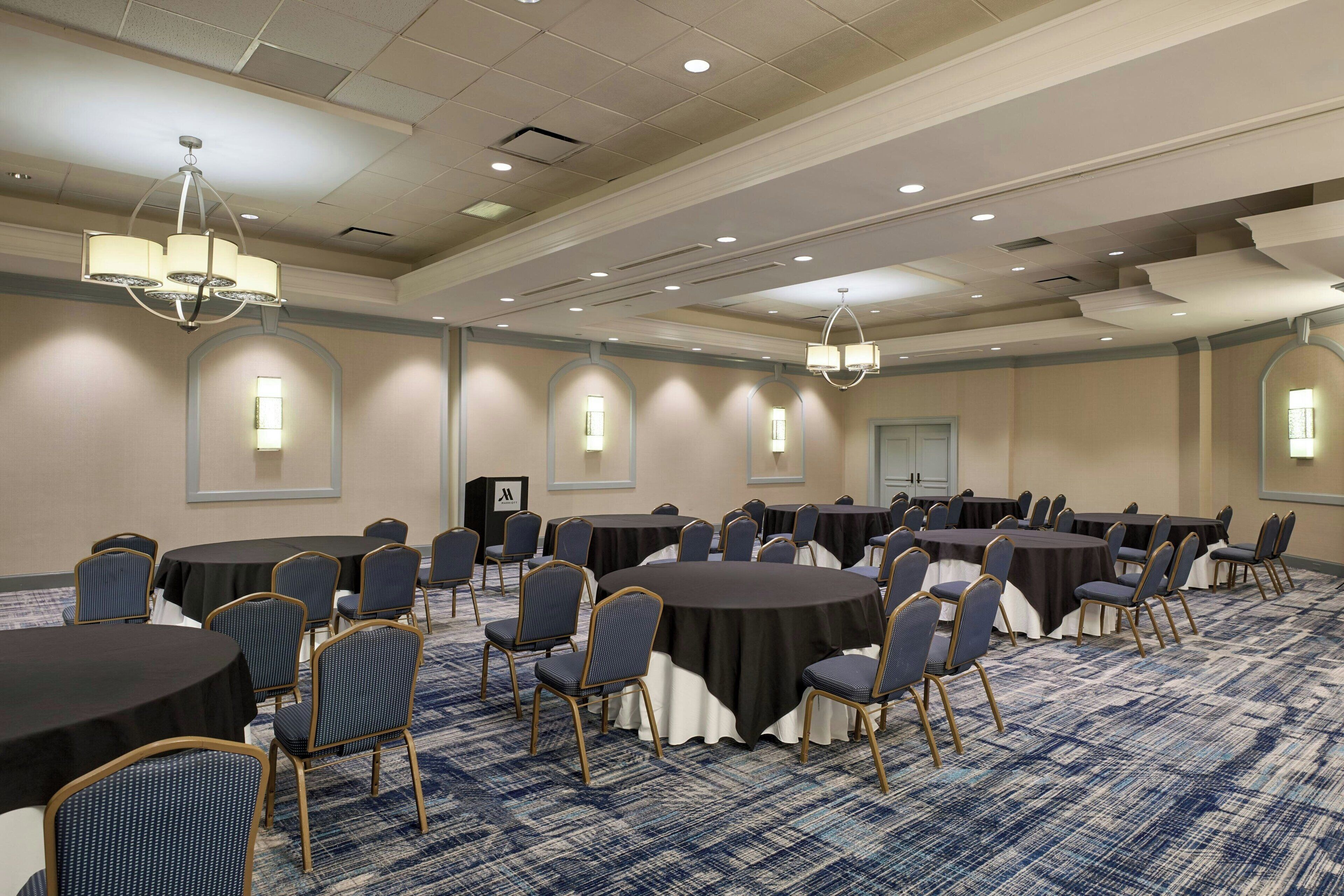 A conference room with round tables, chairs, and chandeliers.