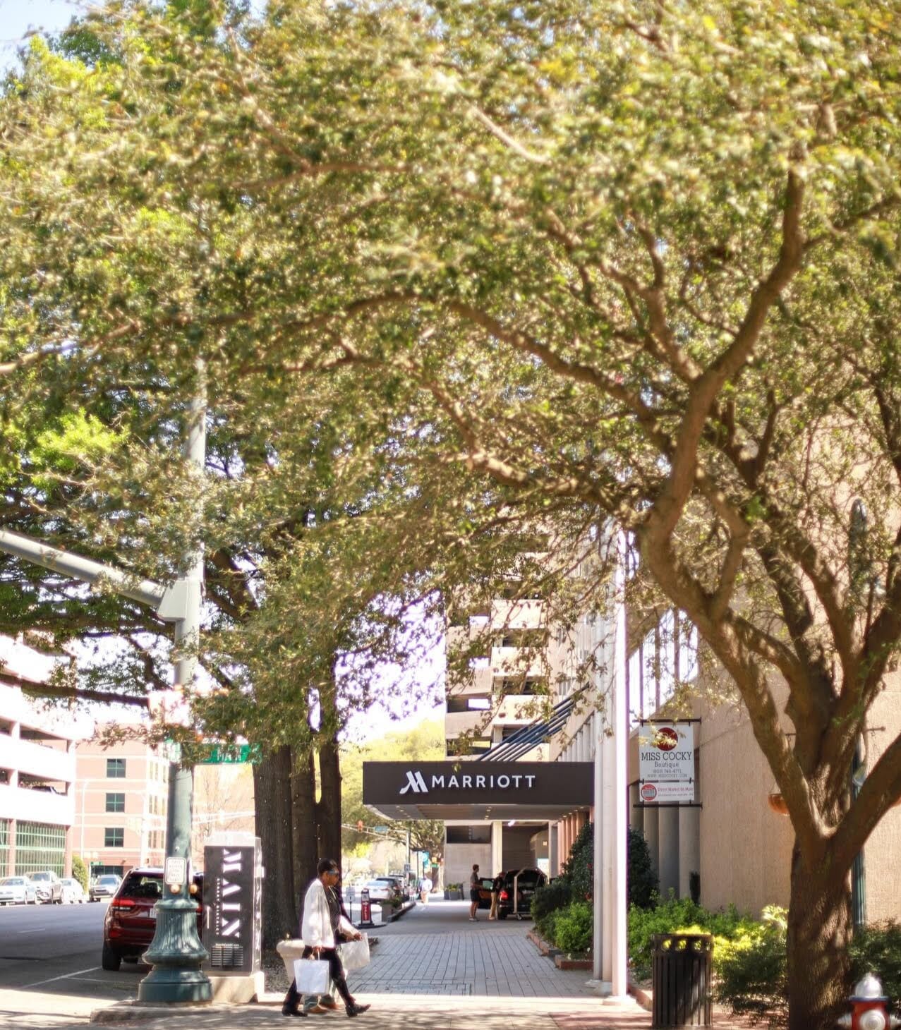 L’entrée d’un hôtel Marriott, avec un trottoir pour piétons, des arbres et des voitures garées.