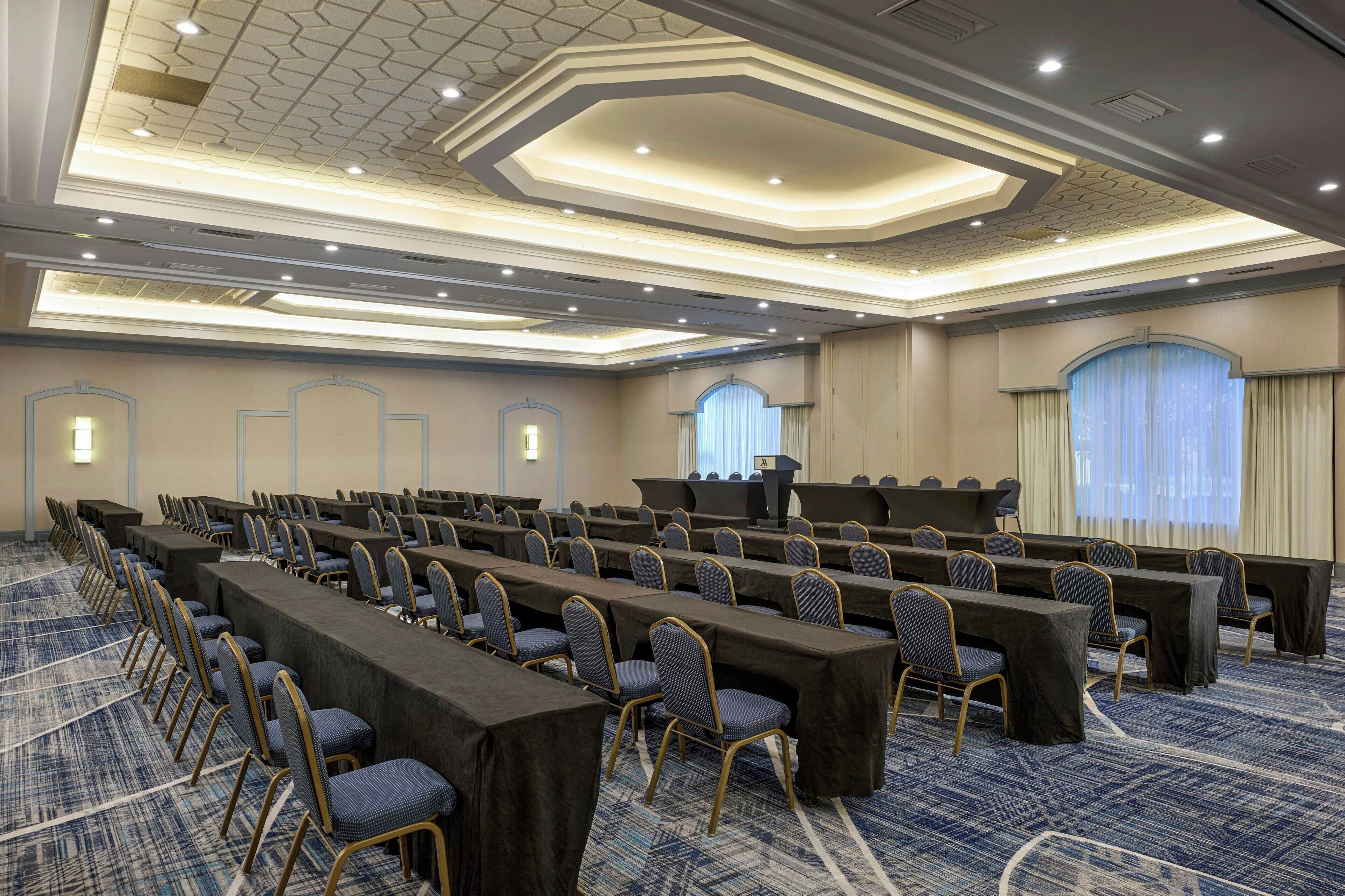A conference room with rows of tables and chairs, a podium, and a carpeted floor.