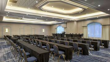 A conference room with rows of tables and chairs, a podium, and a carpeted floor.