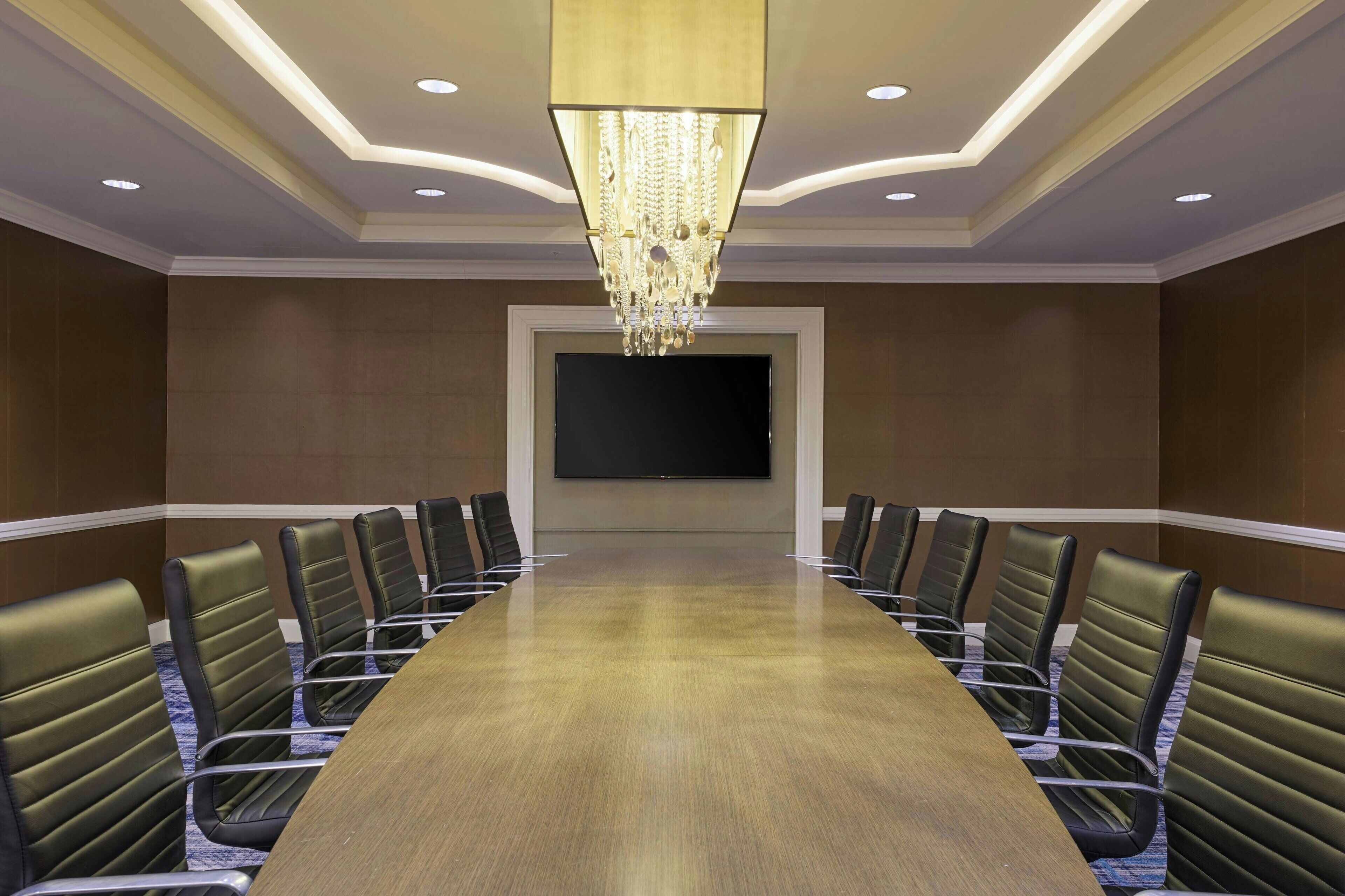 A conference room with a long table, chairs, a chandelier, and a flat-screen TV on the wall.