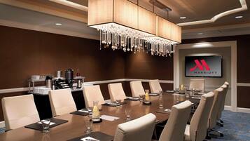 A conference room with a long table, multiple chairs, a chandelier, a coffee station, and a Marriott logo on the wall.