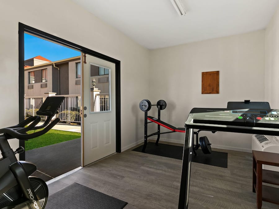 Un gimnasio con equipamiento de ejercicio, cinta de correr y banco para pesas.