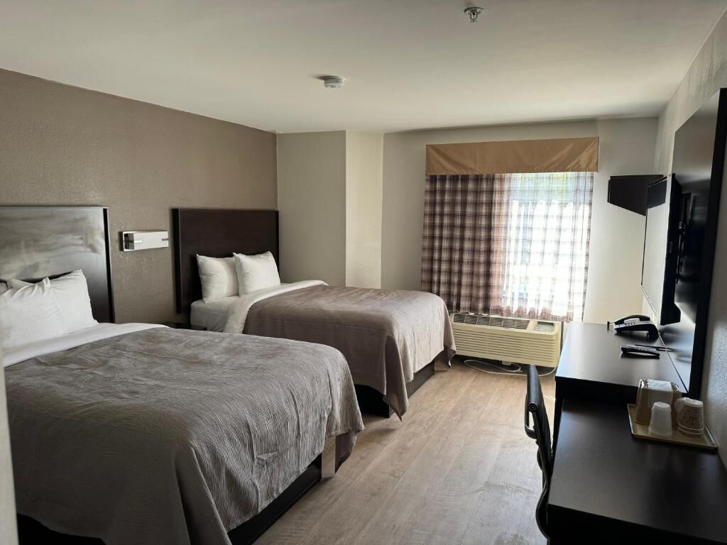 Een hotelkamer met twee bedden, een bureau, een flatscreentelevisie en een raam met gordijnen.
