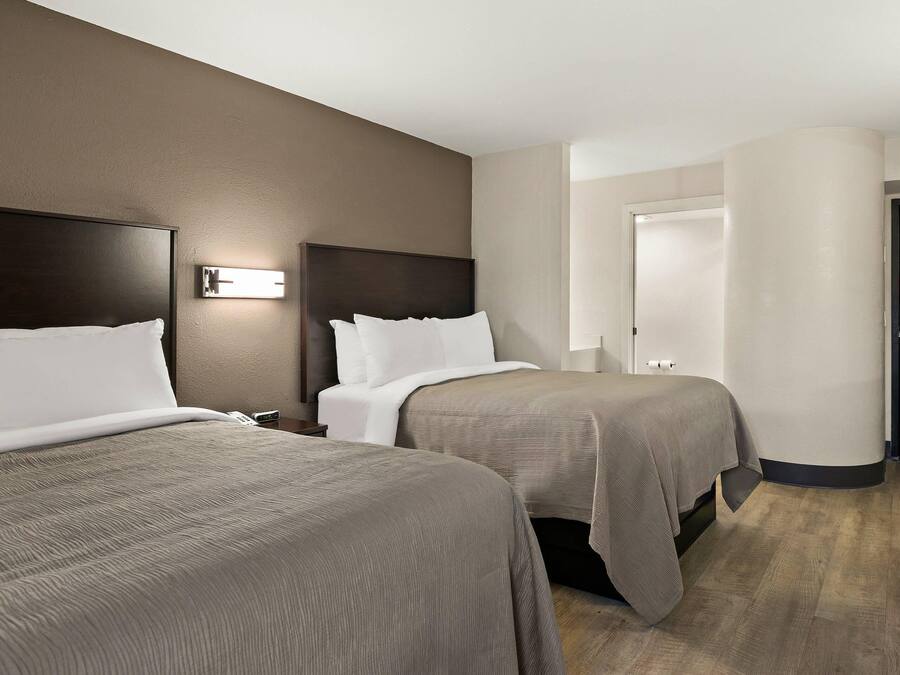 Habitación de hotel con dos camas, una mesita de noche, una lámpara de pared y una puerta.