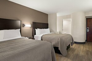 A hotel room with two beds, a nightstand, a wall-mounted light, and a door.