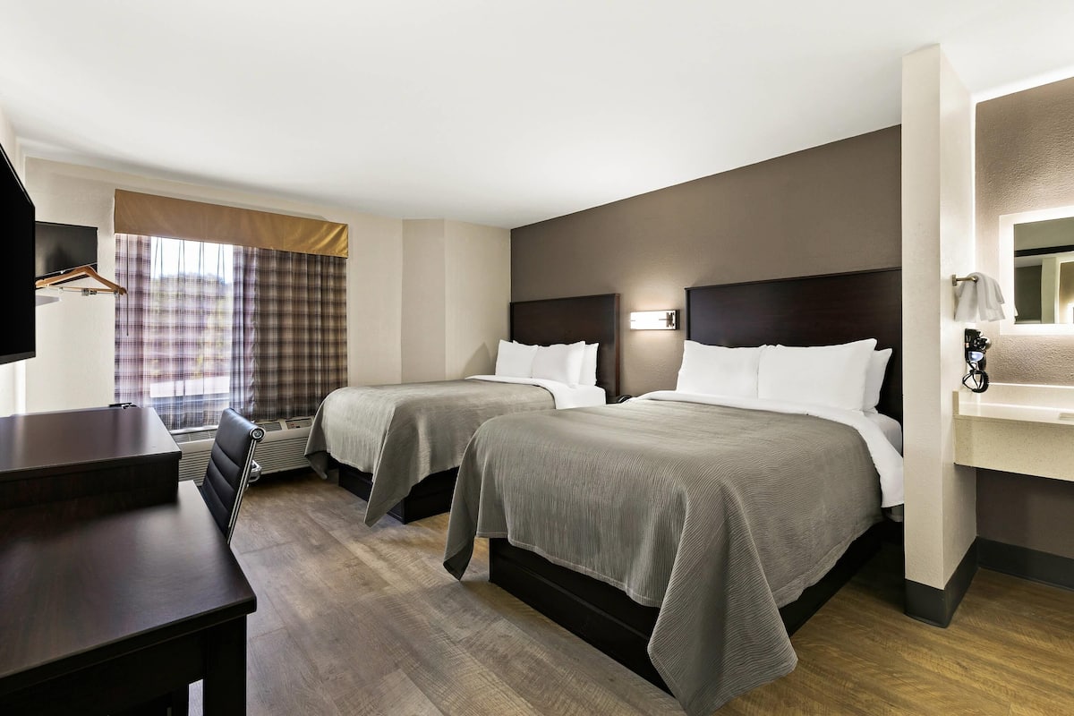 A hotel room with two beds, a desk, a TV, and a window with curtains.