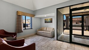 A hotel lobby with a beige sofa, red armchairs, a large window with plaid curtains, and a painting on the wall. - Quality Inn Lavonia I-85 (Lavonia)