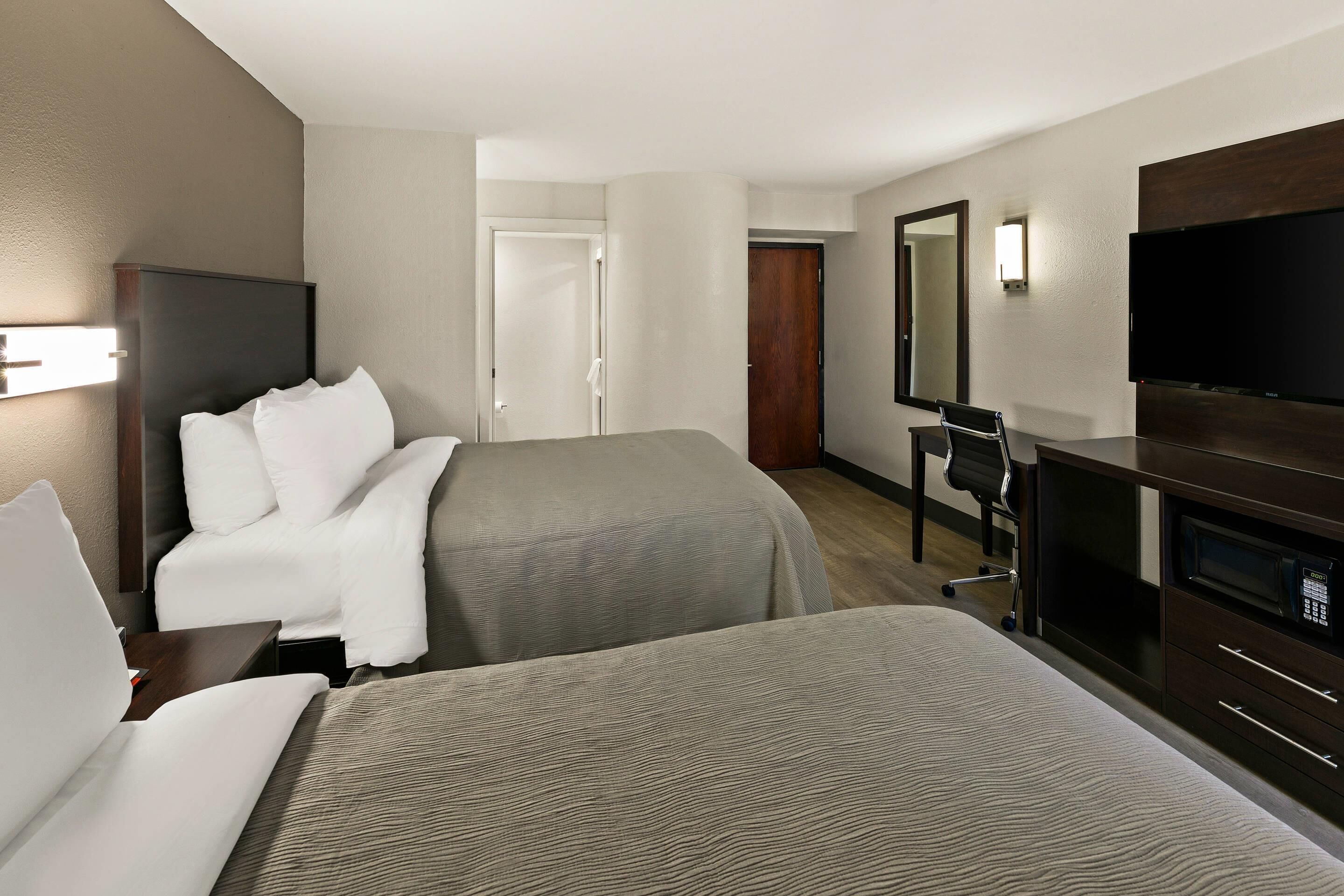 Una habitación de hotel con dos camas, un escritorio, una silla, un televisor y un armario.