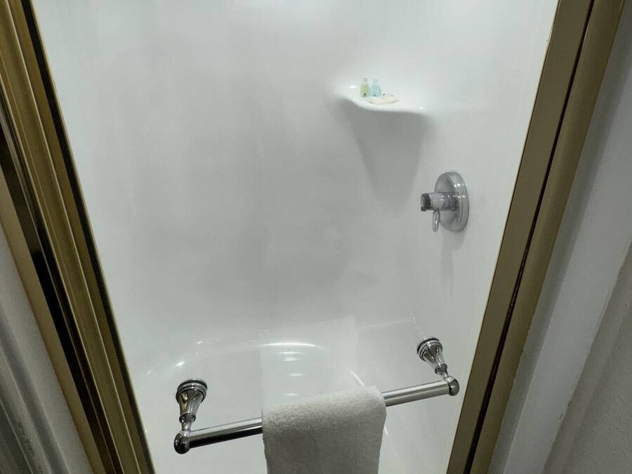 Une salle de bain avec une douche à parois de verre, un porte-serviettes et une étagère contenant des articles de toilette.