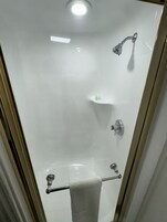 Un baño con cabina de ducha de vidrio, un perchero y un estante con artículos de aseo.
