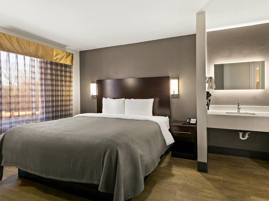 Hotelkamer met een groot bed, nachtkastje met telefoon, badkamer met spiegel en wastafel, en een raam met gordijnen.