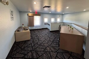 A hotel room with a sofa, a small table, a window with curtains, a radiator, and a patterned carpet.