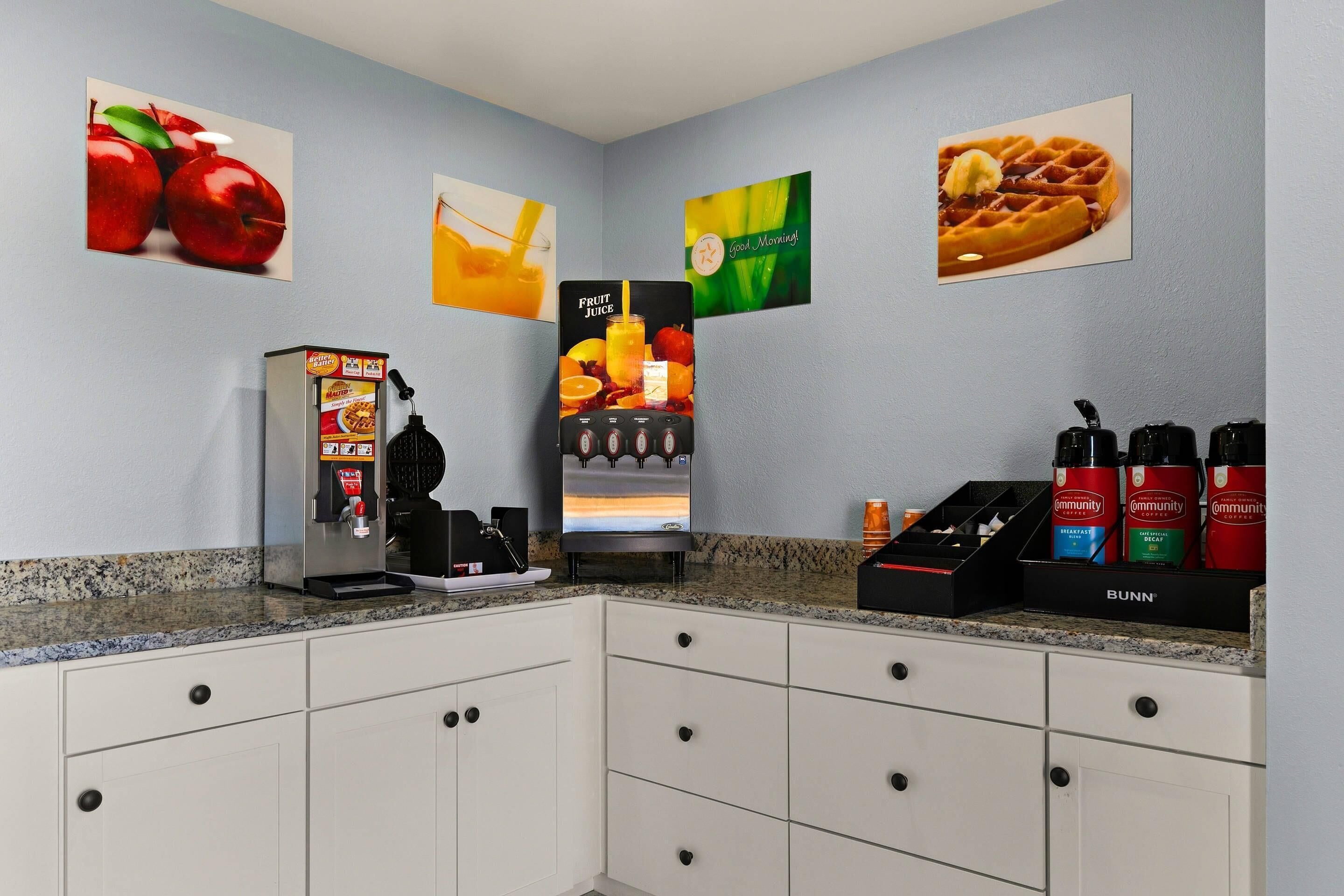 A kitchenette with a coffee machine, a juice dispenser, and a coffee station with branded mugs.