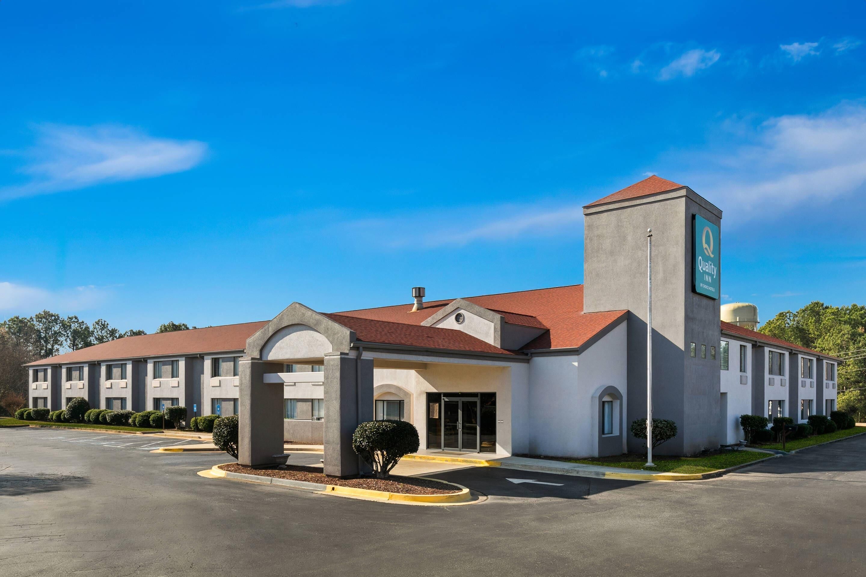 A hotel with a central entrance, multiple windows, and a parking lot.
