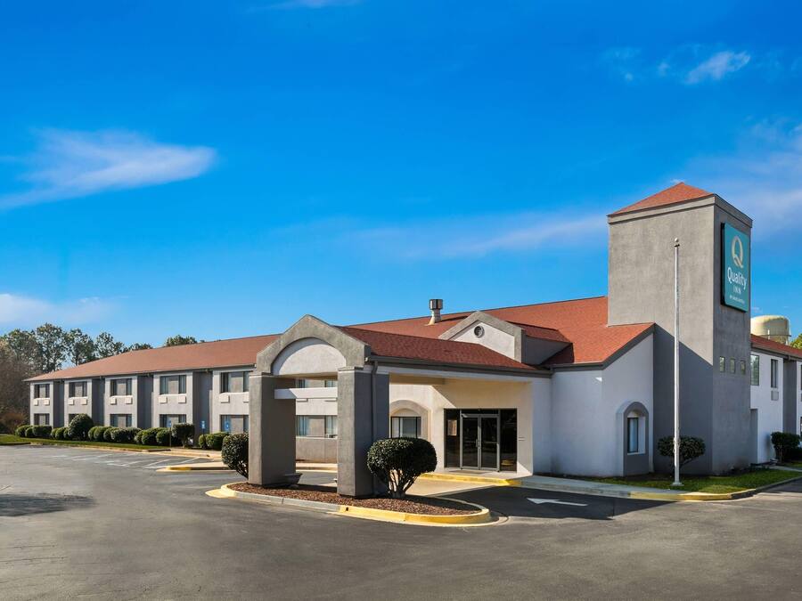 A hotel with a central entrance, multiple windows, and a parking lot.